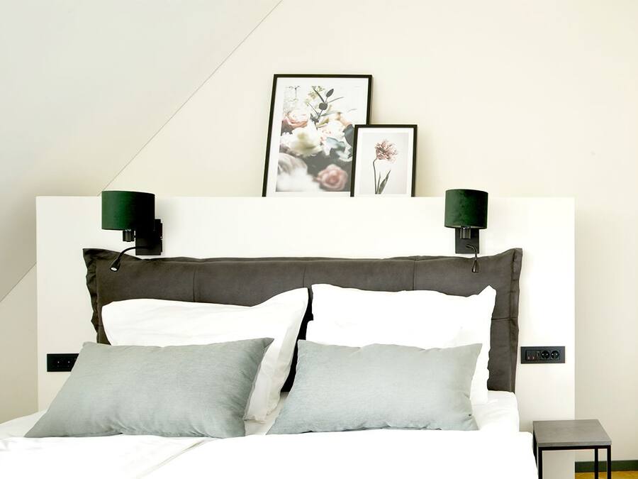 A modern bedroom with a large bed, two wall-mounted lamps, and framed artwork above the bed.