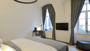 A modern bedroom with a large bed, a desk, a chair, and a TV mounted on the wall. - Garden Rooms (Maribor)