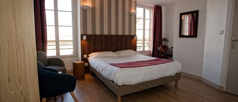 A bedroom with a large bed, a desk, a chair, and a window with curtains.