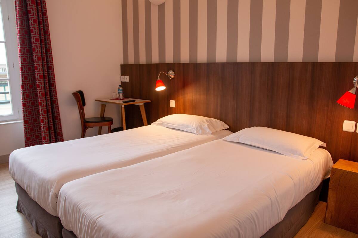 Ein Hotelzimmer mit zwei Betten, einem Schreibtisch, einem Stuhl, einer roten Lampe und einer gestreiften Wand.