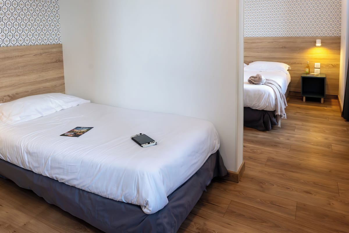 Ein Hotelzimmer mit Holzboden, einem Bett mit weißer Bettwäsche, einem Nachttisch mit Lampe und einem Wandhintergrund mit Muster.