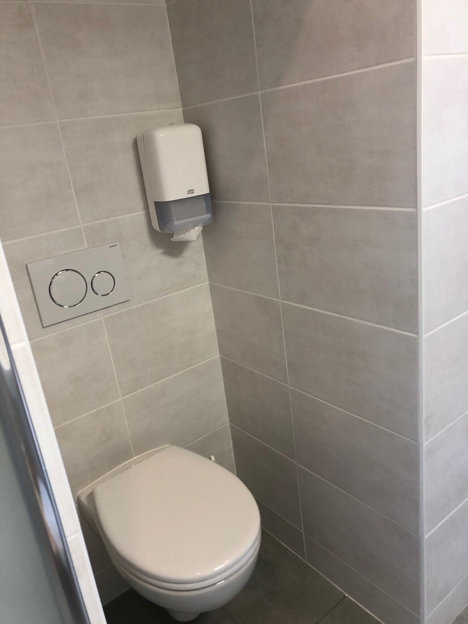 A small, modern bathroom with a toilet, a hand dryer, and a flush button.
