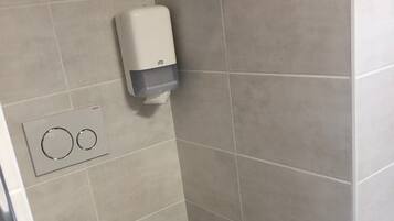 A small, modern bathroom with a toilet, a hand dryer, and a flush button.