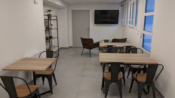 A conference room with multiple tables and chairs, a large flat-screen TV on the wall, and a window with blinds.