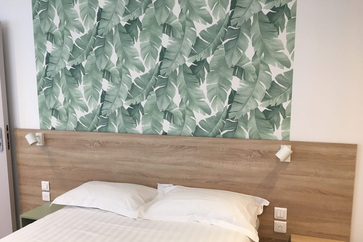 Ein Bett mit weißer Bettwäsche, einem hölzernen Kopfteil und einer Wand mit einem Blattmuster.