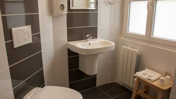 Une salle de bain équipée de toilettes, d’un lavabo et d’un petit tabouret en bois, ainsi que d’une serviette et d’articles de toilette.
