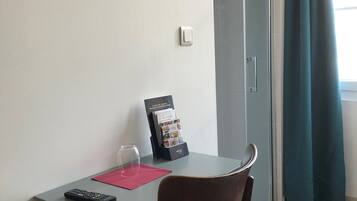 Un pequeño comedor con una mesa, una silla, un control remoto, un vaso y un atril para folletos.
