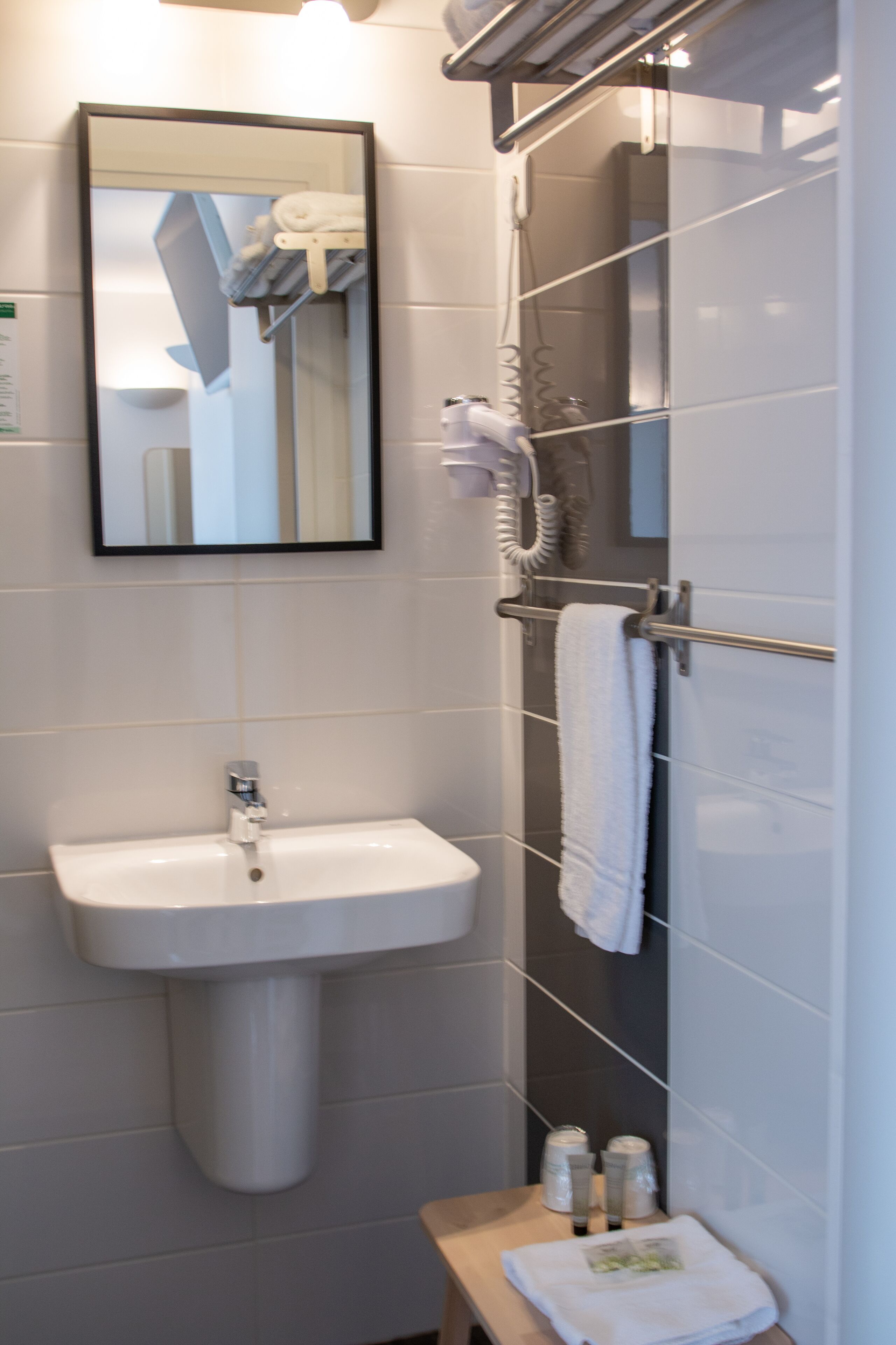 A bathroom with a sink, mirror, towel rack, and shower.