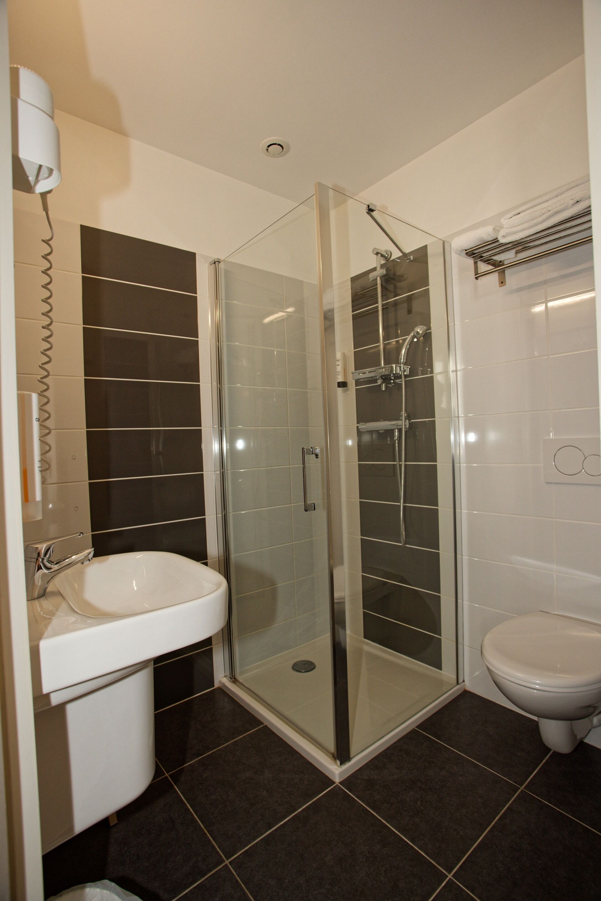 Un baño moderno con ducha envuelta en vidrio, lavamanos blanco y un inodoro.