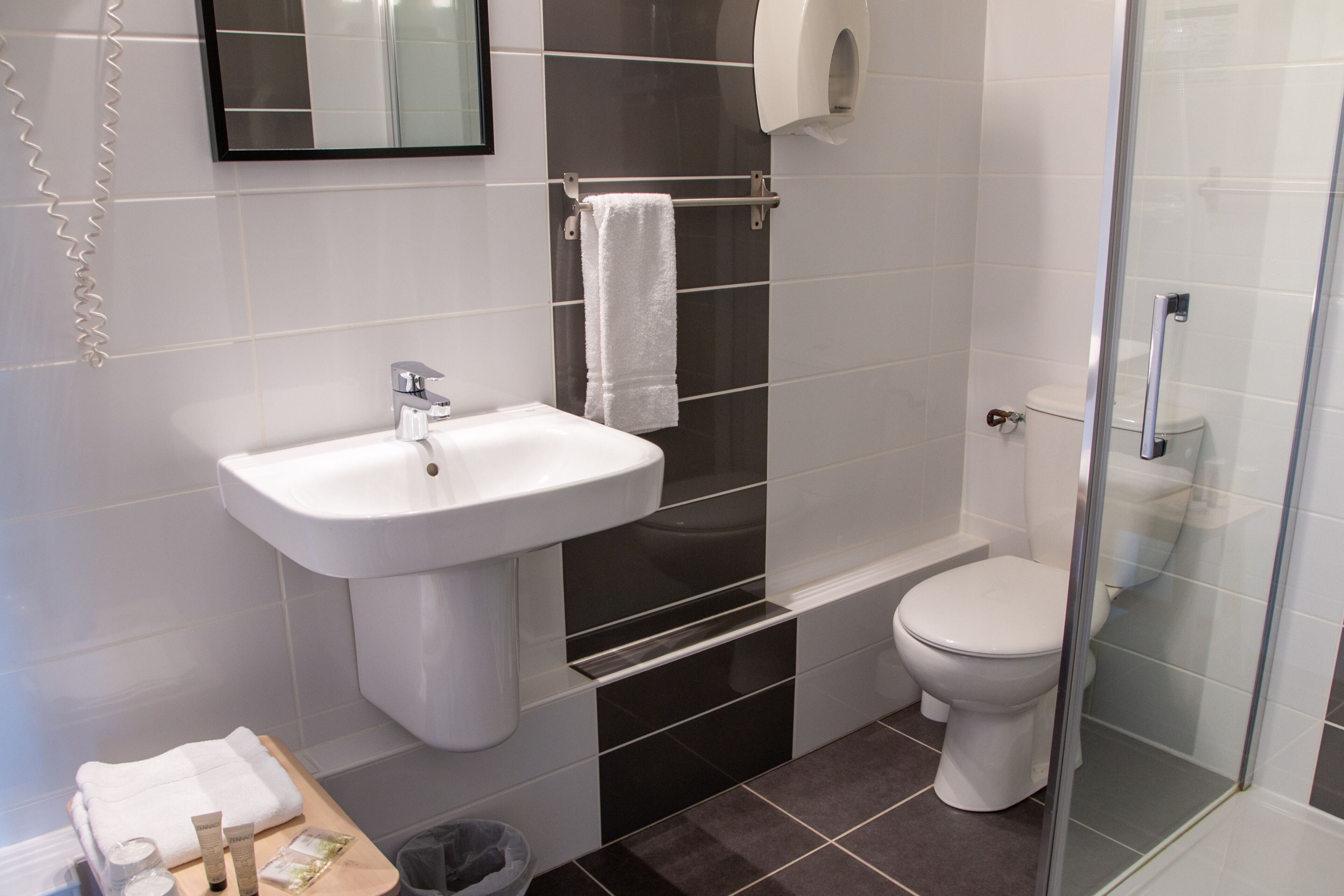 A modern bathroom with a white sink, a glass shower enclosure, and a toilet.