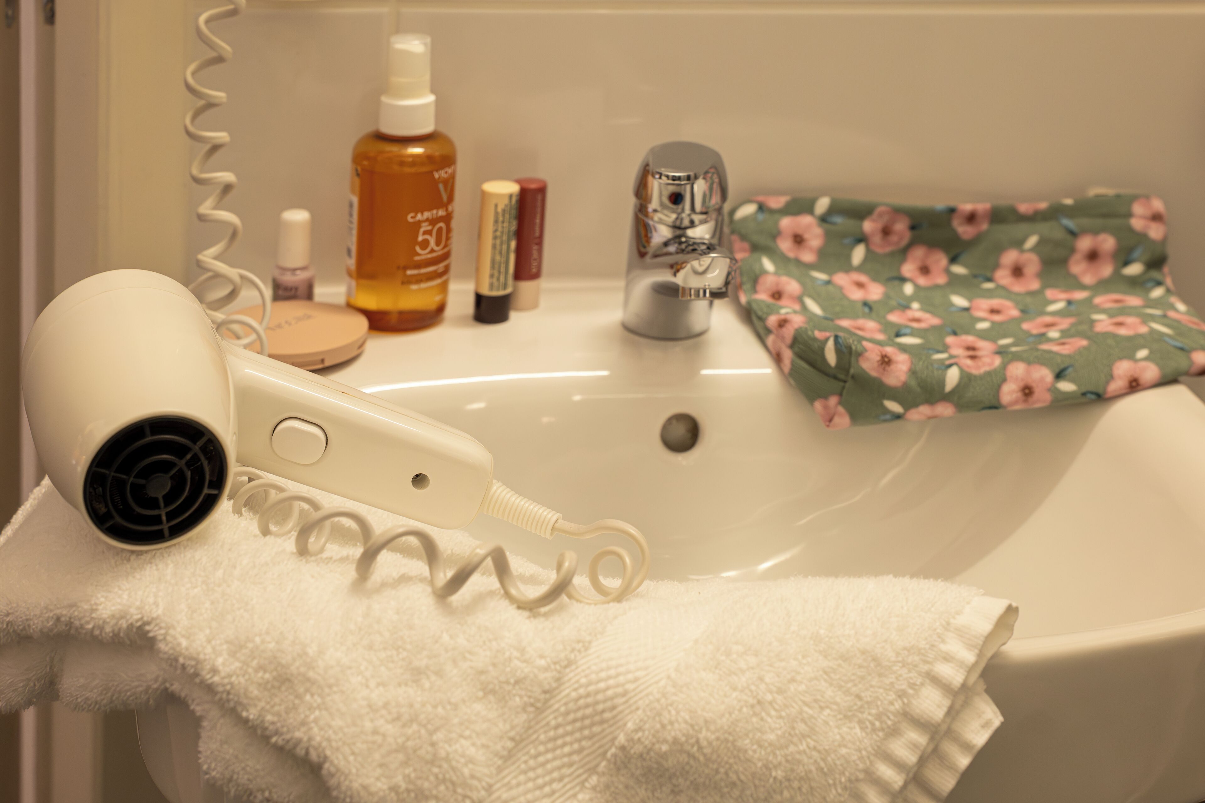 A bathroom with a white sink, a hairdryer, and toiletries on the counter.