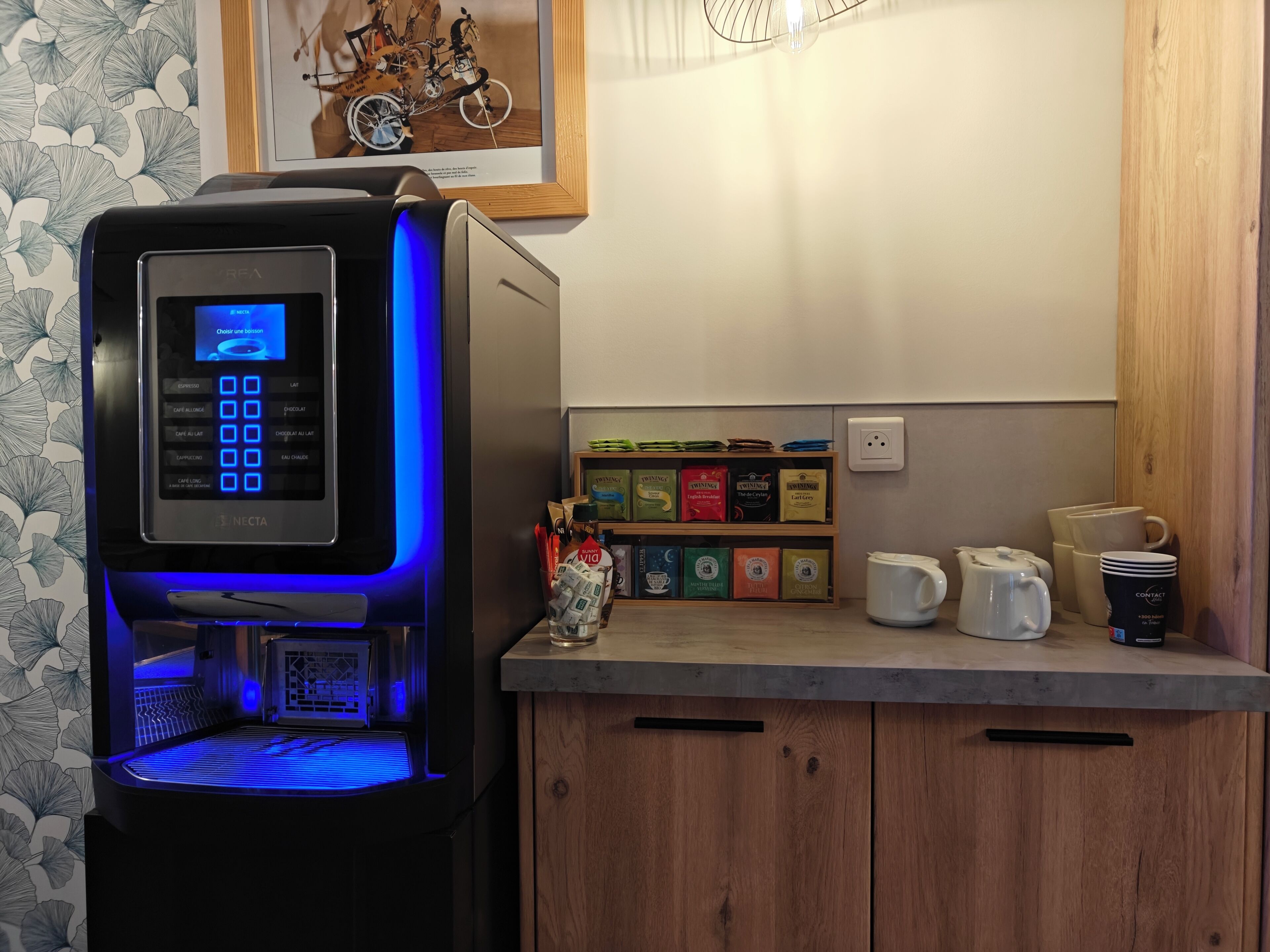 Eine kleine Küche mit Kaffeemaschine, Kaffeezubereiter und einer Ablage für Kaffeekapseln.