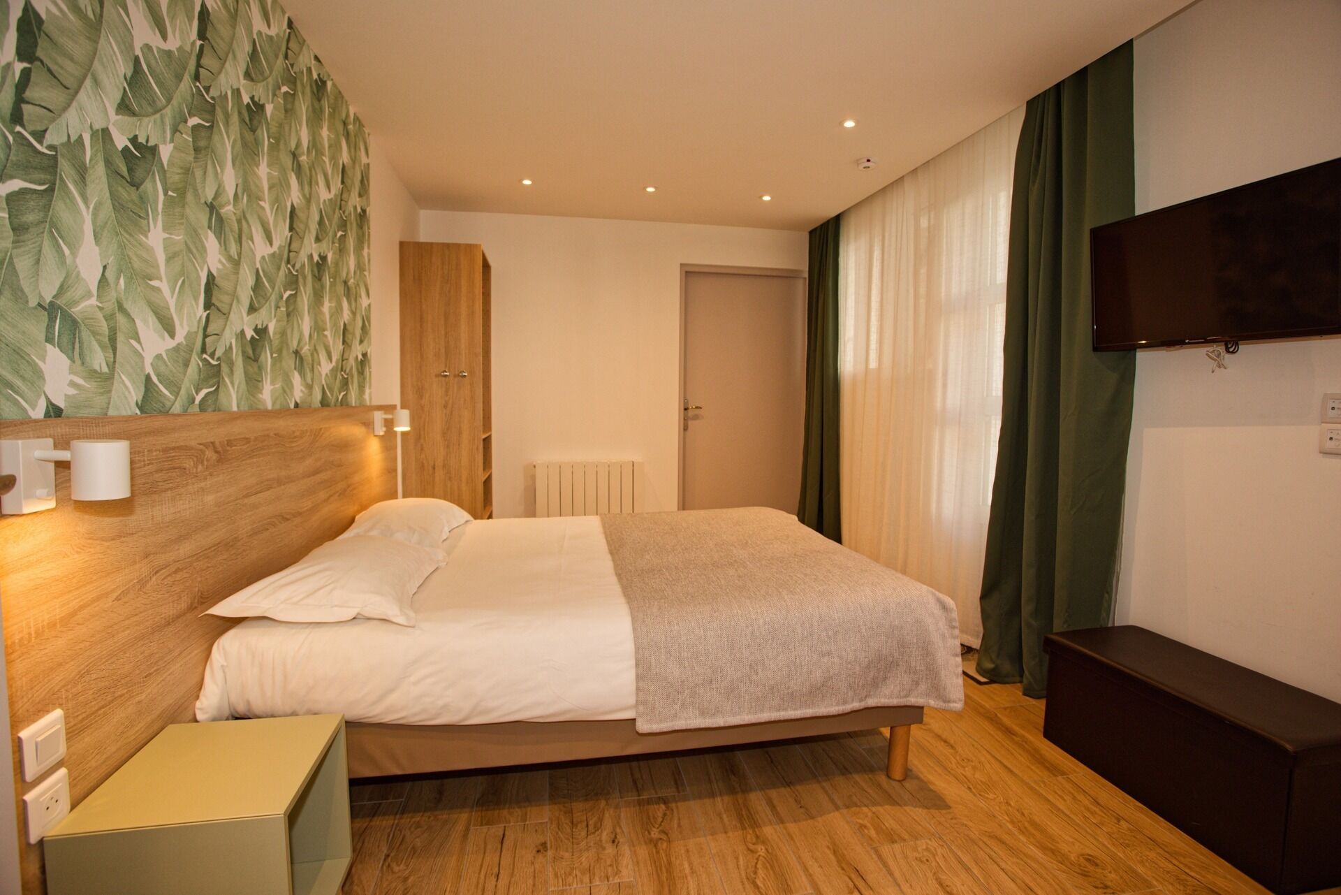 A hotel room with a bed, a bedside table, a TV mounted on the wall, and a wooden headboard.