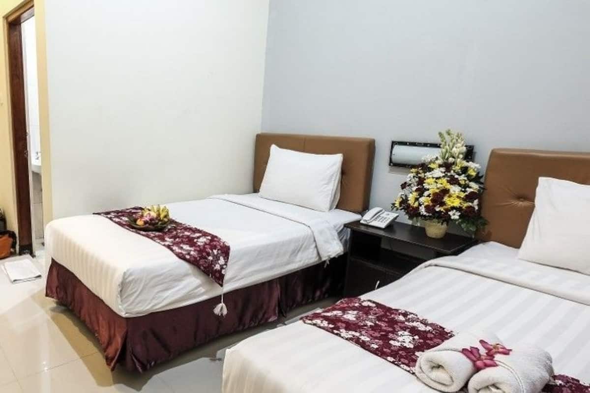 Une chambre d’hôtel avec deux lits, une porte en bois, un bureau avec un magazine et une table de chevet avec un téléphone et des fleurs.