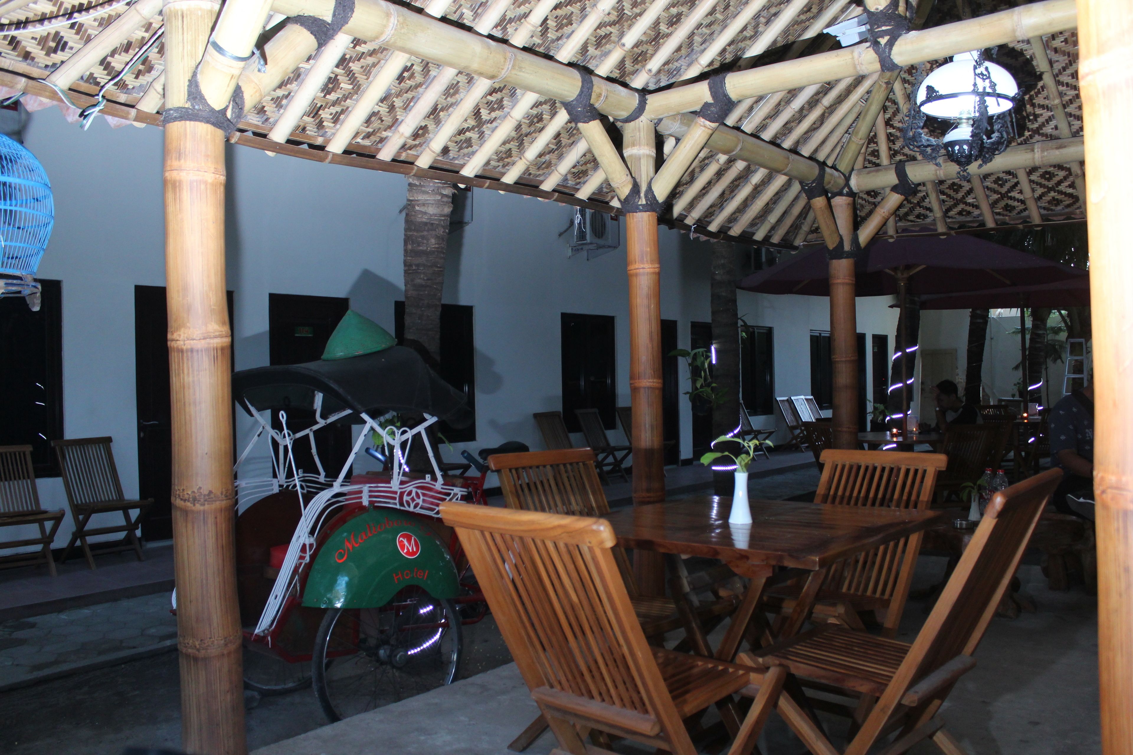 An outdoor seating area with bamboo structures, wooden tables and chairs, and a bicycle with a green seat.