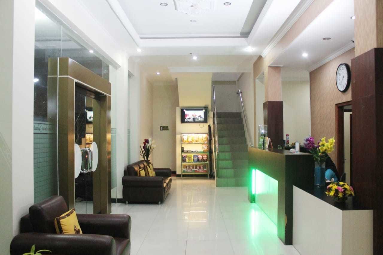 A hotel lobby with a reception desk, a staircase, a sofa, and a television.