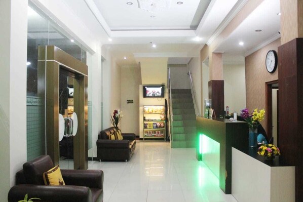 A hotel lobby with a reception desk, a staircase, a sofa, and a television. - Malioboro Garden Hotel (Yogyakarta)