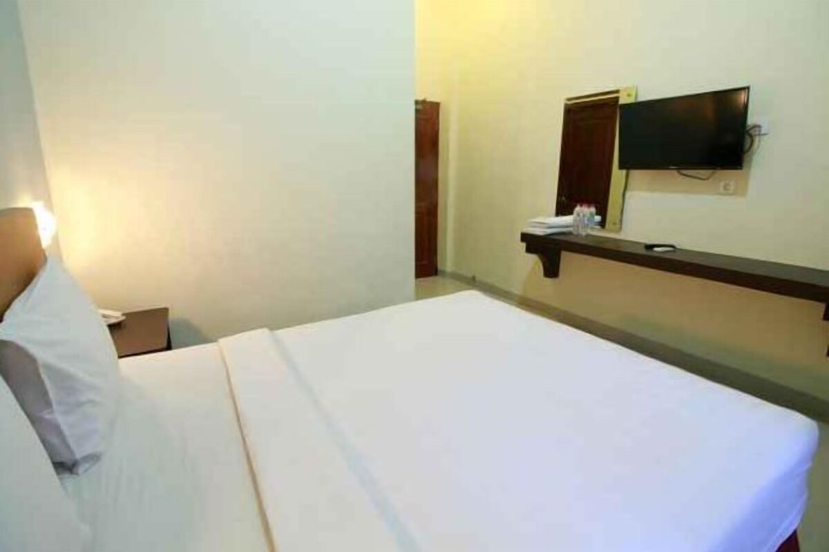 Een hotelkamer met een bed, een nachtkastje, een aan de muur bevestigde televisie en een deur die naar een andere kamer leidt.