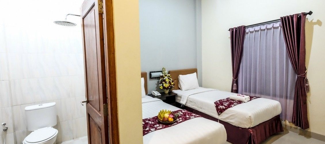 A hotel room with two beds, a shower, a toilet, and a nightstand with a phone and flowers.