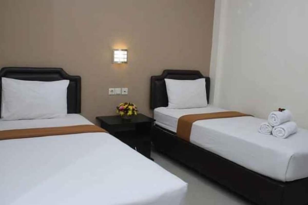 A hotel room with two beds, a nightstand with a vase of flowers, and a wall-mounted light.