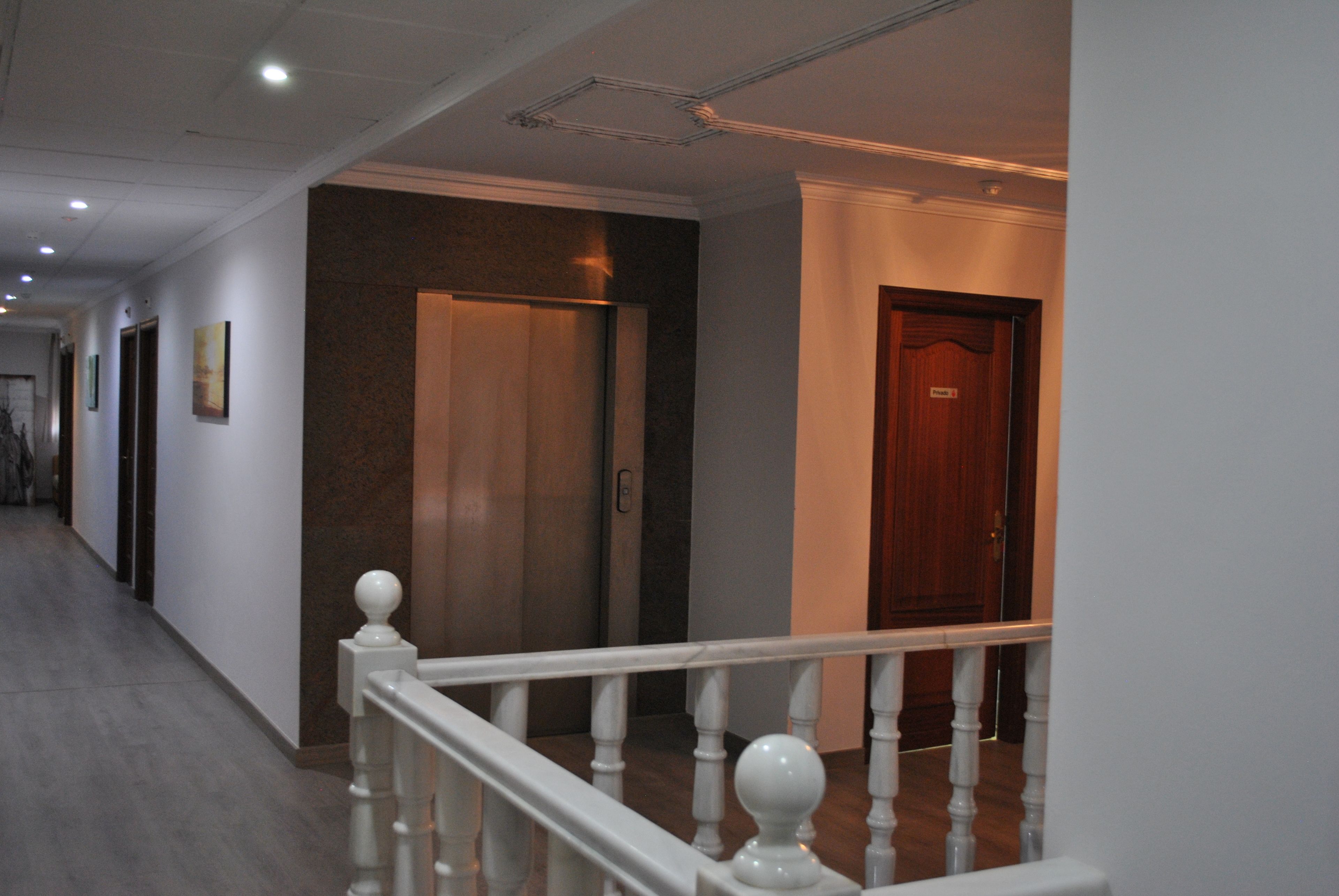 Un couloir d’hôtel avec une porte en bois, une rambarde blanche et un passage avec un plancher en bois.