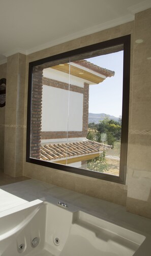 A bathroom with a large window, a bathtub, and a view of a building and landscape. - Hotel Restaurante Dama de Baza (Baza)