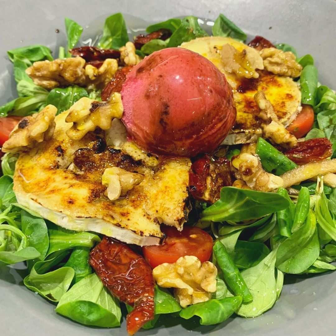 A salad with grilled chicken, walnuts, tomatoes, and a red apple on a bed of green leaves.