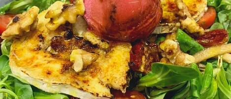 A salad with grilled chicken, walnuts, tomatoes, and a red apple on a bed of green leaves.