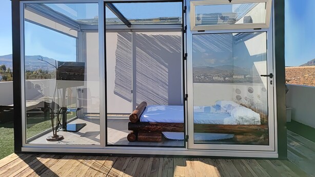 A modern room with a sliding glass door, a wooden floor, and a bed with a white cover. - Hotel Restaurante Dama de Baza (Baza)