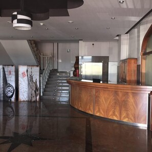 A modern lobby with a curved reception desk, a staircase with metal railings, and a large window. - Hotel Restaurante Dama de Baza (Baza)