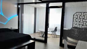 A modern hotel room with a large bed, a desk, and a view through a sliding door to a balcony with a chair. - Hotel Restaurante Dama de Baza (Baza)