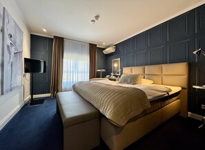 A modern hotel room with a large bed, a bench, a flat-screen TV, and a large window with curtains. - Parkhotel Bielefeld (Bielefeld)