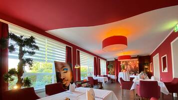 Interior de restaurante con paredes rojas, mesas blancas y sillas rojas.