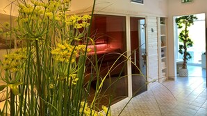 Een hotellobby met een grote kamerplant, een rode zithoek en een trap naar een hoger niveau.