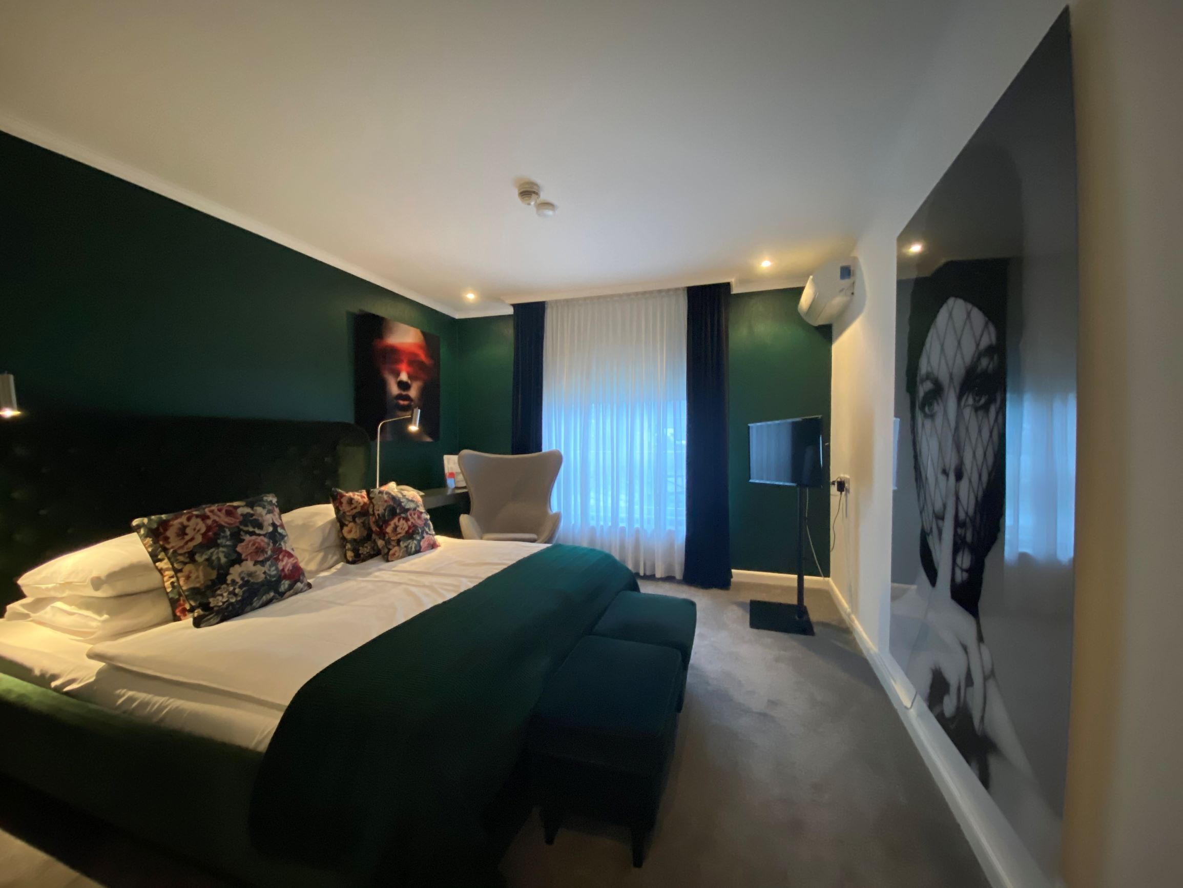 Ein modernes Schlafzimmer mit einem großen Bett, einem Nachttisch, einem Sessel und einem an der Wand befestigten Fernseher.