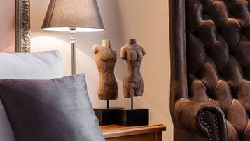 A bedroom with a bed, a lamp, two wooden sculptures, a dark brown leather armchair, and a wooden nightstand.