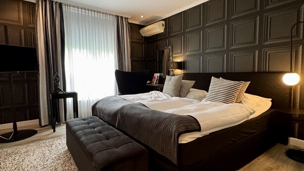 Een moderne hotelkamer met een groot bed, een bank, een flatscreen televisie en een wandairconditioner.