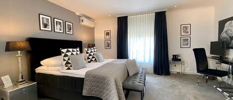 Una habitación de hotel moderna con una cama grande, un escritorio y una silla. Hay cuadros enmarcados en la pared y una ventana con cortinas.