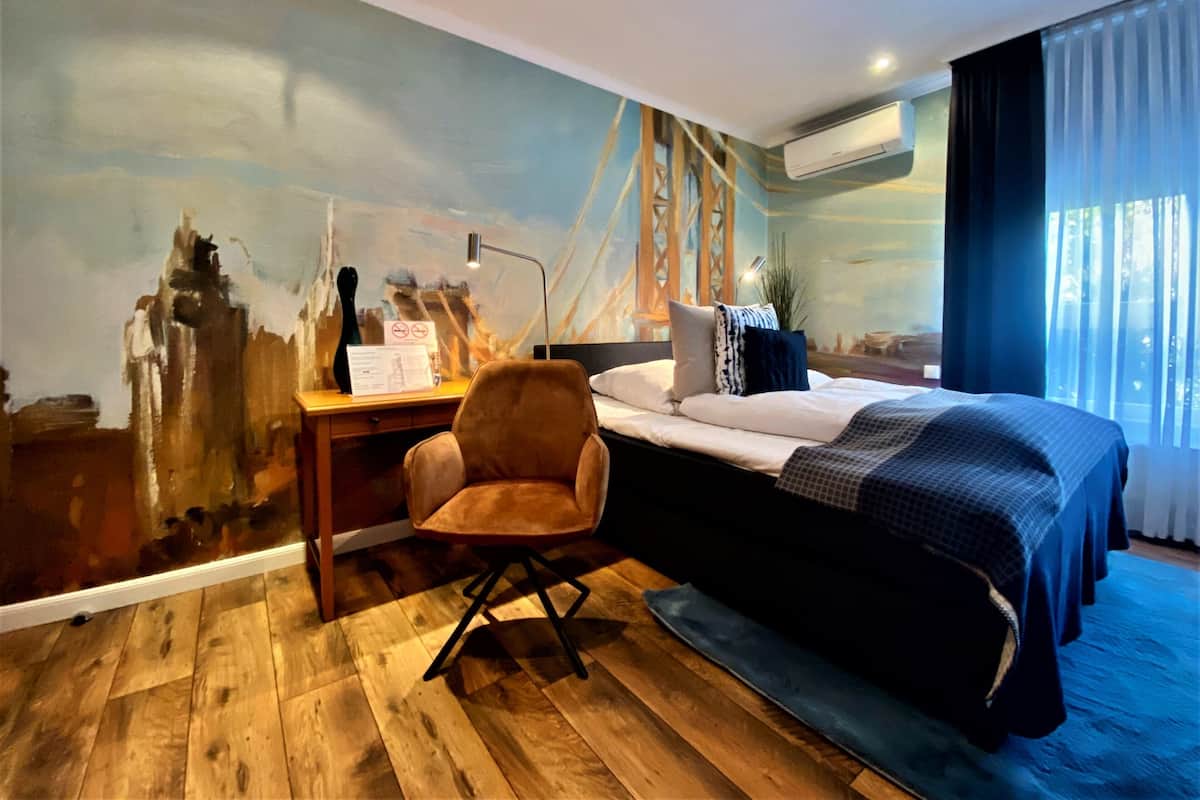 Une chambre d’hôtel équipée d’un lit, d’un bureau, d’une chaise, d’une décoration murale et d’un appareil de climatisation.