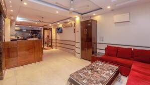 Un vestíbulo de hotel con mostrador de recepción, un sofá rojo, un armario de madera, un ventilador de techo y un televisor montado en la pared.
