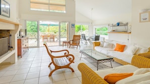 A spacious living area with a fireplace, a sofa, a coffee table, and a dining table. There is a balcony with outdoor seating and a view of greenery. - Villa avec Piscine Privée | WiFi Gratuit + Parking (Moliets)