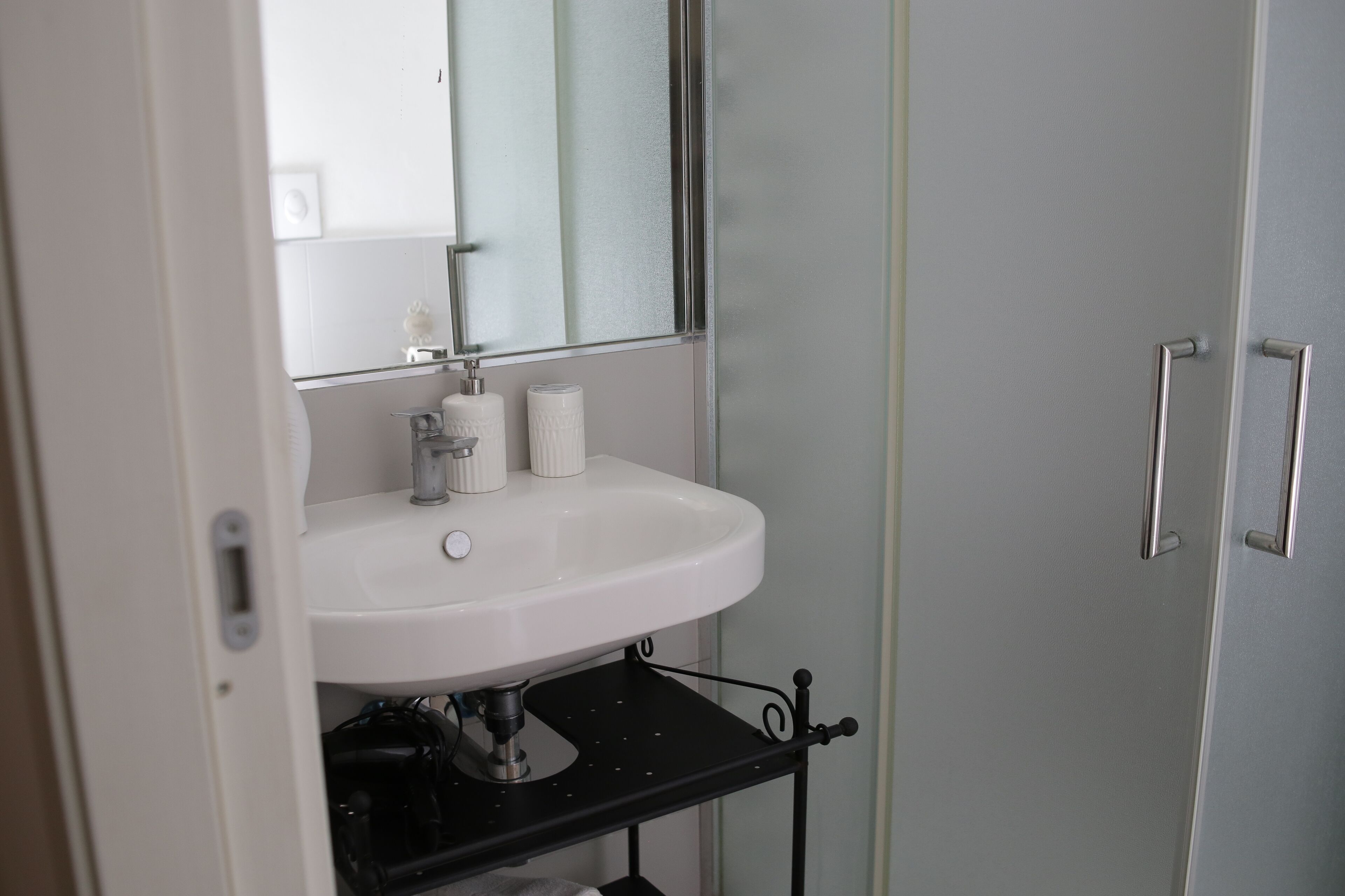 A bathroom with a white sink, a mirror, and a black shelf below the sink.