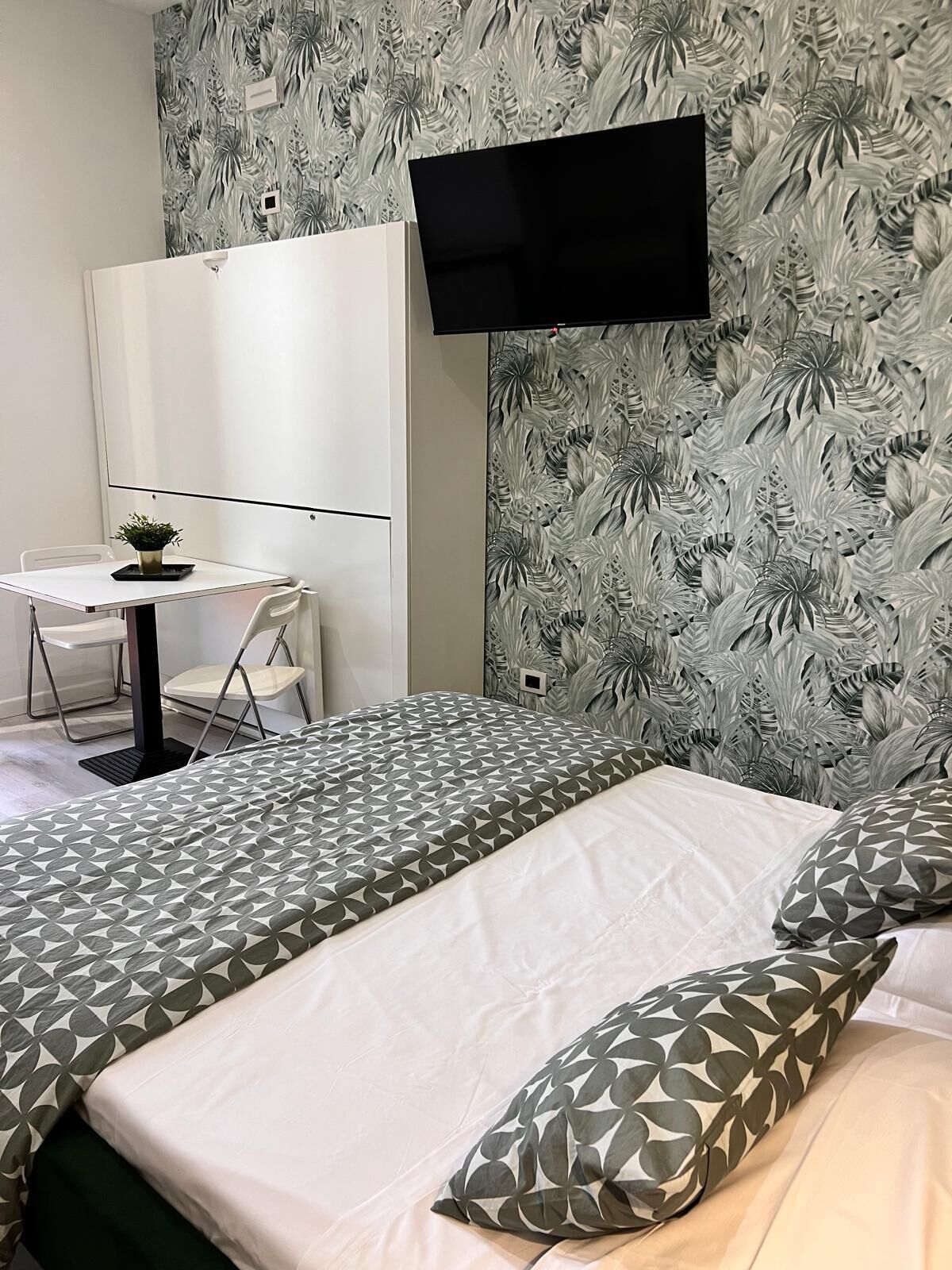 A hotel room with a bed, a desk, and a TV mounted on the wall.