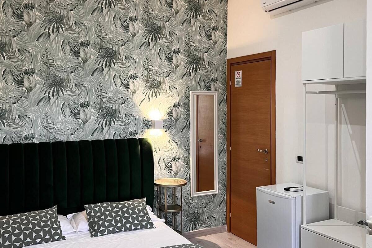 A bedroom with a bed, a nightstand, a mirror, a wardrobe, and an air conditioning unit.