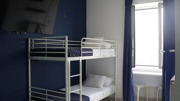 A bunk bed room with a TV on the wall, a window with curtains, and a small white chair.