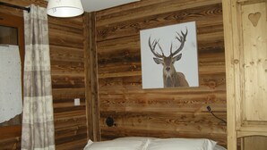 A wooden cabin room with a bed, a wall-mounted lamp, and a framed deer picture. - 100 m2 col du Télégraphe 4**** for 10 people in the center of Valloire (Valloire)