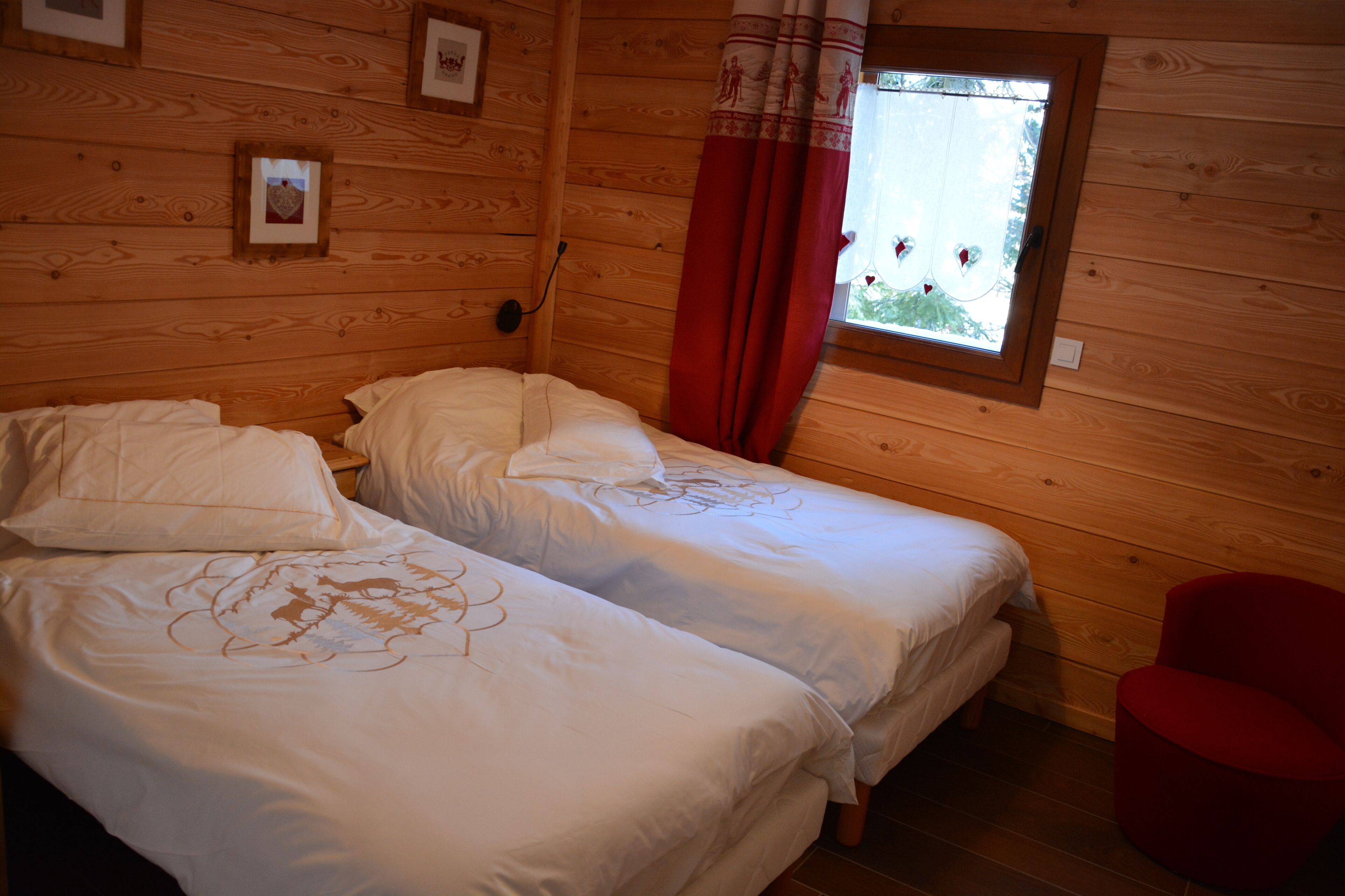 Une chambre de style cabane avec deux lits, une fenêtre avec des rideaux rouges et des murs en bois.