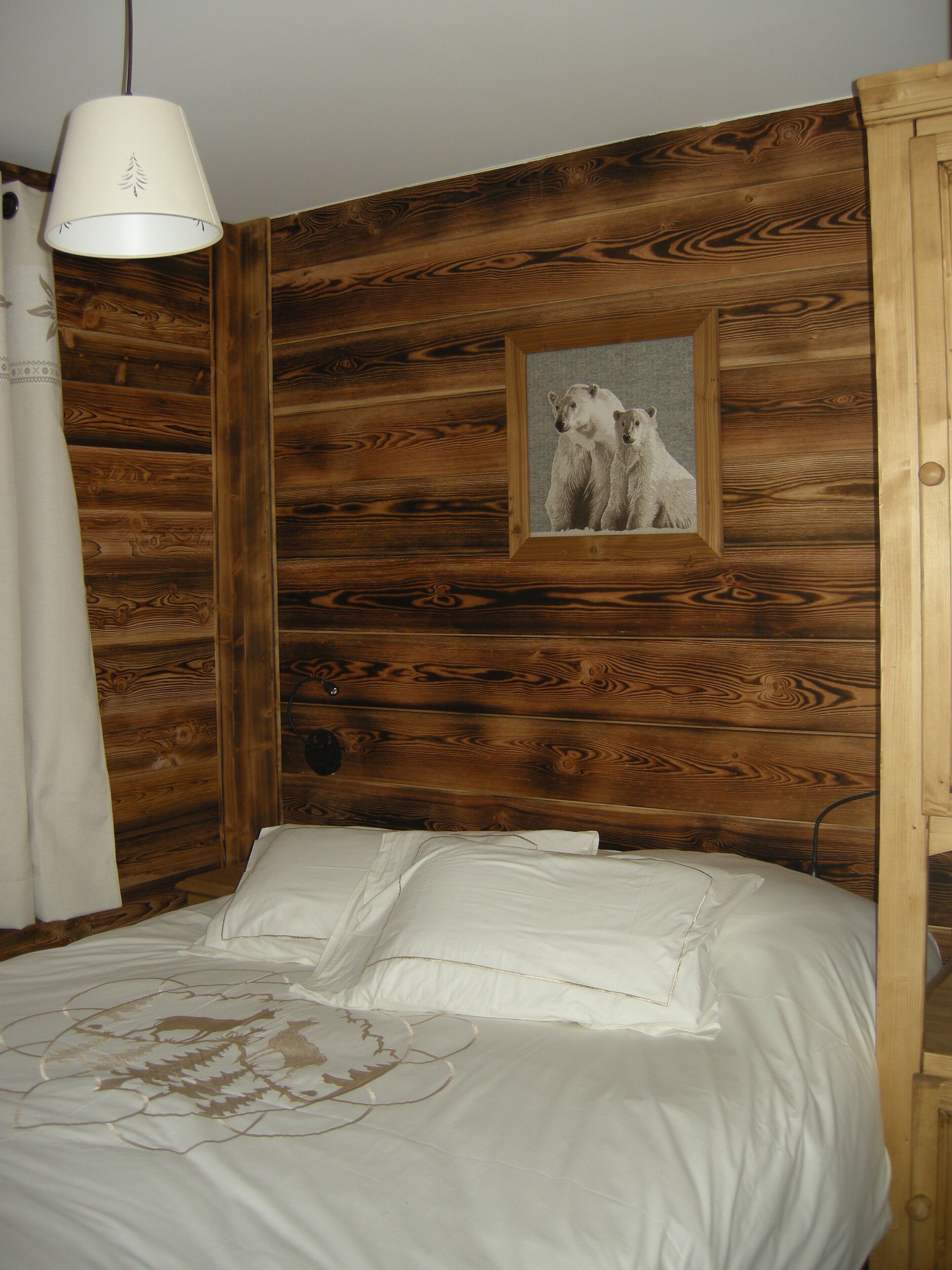 Una habitación estilo cabaña de madera con una cama, un cuadro enmarcado de osos y una lámpara colgante.