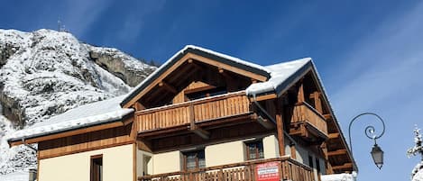 A multi-story building with balconies, a sign for a grill and pasta cafe, and snow-covered surroundings.