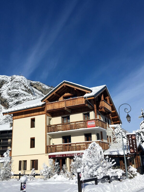 A multi-story building with balconies, a sign for a grill and pasta cafe, and snow-covered surroundings.
